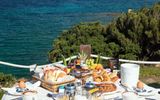 Frühstückstisch auf einer Terrasse mit traumhaftem Blick auf das tiefblaue Meer – serviert werden frische Croissants, Brötchen, Obst, Säfte und Kaffee – ein perfekter Start in den Tag mit mediterranem Panorama.