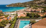 Panoramablick auf eine traumhafte Bucht mit türkisblauem Meer, feinem Sandstrand und malerischem Küstenort – im Vordergrund ein Hotelpool mit Liegestühlen.