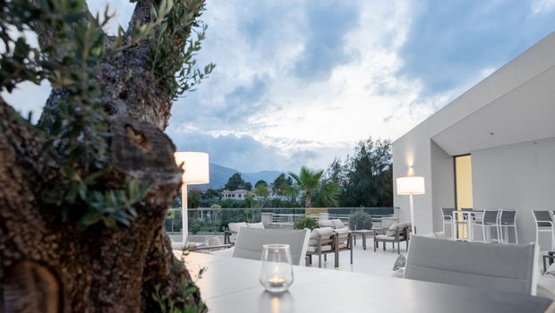 Moderne Terrasse mit eleganten Loungemöbeln, dezentem Licht und Blick auf Palmen, Bäume und umliegende Hügel – klare Linien und stilvolles Ambiente in sanften Farben.