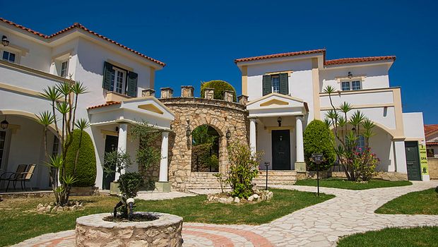 Charmante Hotelanlage im mediterranen Stil mit liebevoll gepflegtem Garten, hellen Fassaden und einem dekorativen Rundbogen aus Naturstein.