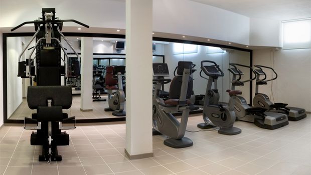 Heller Fitnessraum mit modernen Cardiogeräten, Kraftstation und großen Spiegeln – ideal für sportlich aktive Urlaubsgäste.