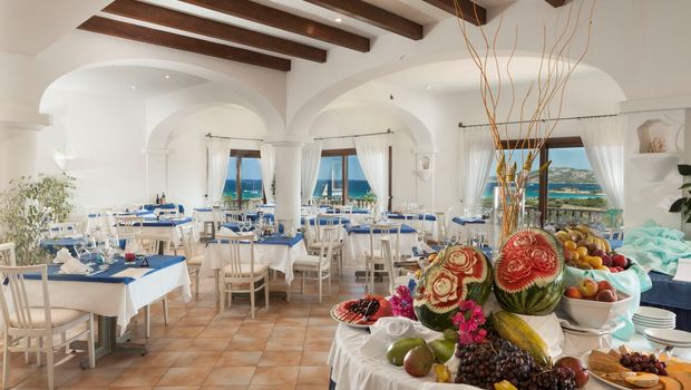 Elegantes Hotelrestaurant mit mediterranem Flair, hellen Bögen und Meerblick – liebevoll gedeckte Tische mit blauen Akzenten und kunstvoll arrangiertes Obstbuffet sorgen für ein stilvolles Ambiente.