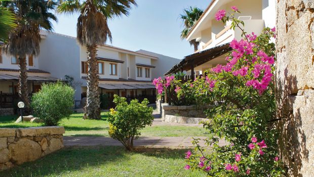 Gepflegte Gartenanlage mit blühenden Bougainvilleen, Palmen und mediterraner Architektur – einladende Umgebung für einen entspannten Aufenthalt.