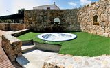 Kleiner Whirlpool im Freien, eingebettet in eine charmante Steinmauer mit rustikalem Flair – umgeben von Kunstrasen und mediterranem Ambiente für entspannte Momente unter freiem Himmel.