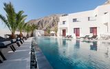Moderner Poolbereich mit stilvollen Liegen und Palmen, umgeben von weißer Architektur und beeindruckender Bergkulisse – ideal zum Entspannen unter der griechischen Sonne.